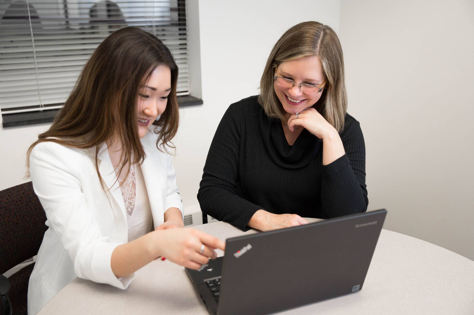 Image of two faculty members huddled around a laptop and reviewing digital materials
